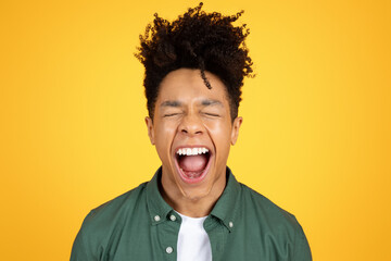 Young black man shouting out of joy, yellow background