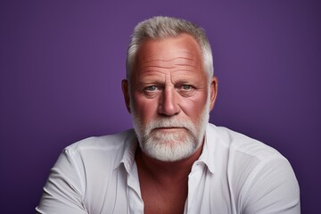 Portrait of a senior man with grey beard and mustache. Studio shot against purple background.