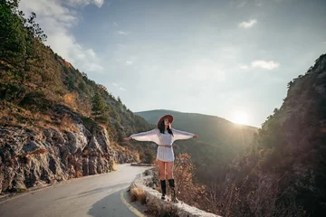 Poster Woman road mountain. A woman in a white sweater, black boots and a hat walks along a winding alpine path between the mountains at sunset in late summer. The concept of travel. © svetograph
