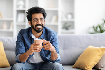 Joyful Indian man holding coffee cup with both hands and looking away - Powered by Adobe
