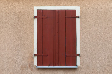 Red closed wooden shutter with white frame, wall beige painted, space for text, no person