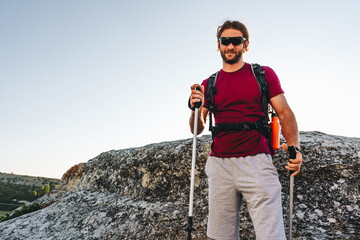 Young man hiker travels through the mountains with trekking poles for nordic walking