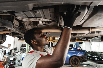 Young African mechanic in uniform working under the car in car service center
