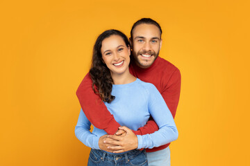 Portrait of loving millennial couple posing on orange background