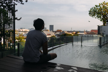 Back side of asian man sitting at poolside in summer, thinking something, silhouette photos,...