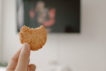 Image of woman hand holding bitten cookie biscuit while watching tv, eating and spending time on white bed in free day. lifestyle concept.