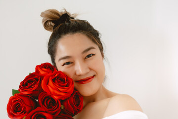 Close up of pretty asian Thai woman holding red roses on valentines day, taking selfie with happy smiling, receiving flowers from boyfriend, isolated over white background wall. 