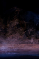 Conceptual image of multi-colored smoke isolated on dark black background and wooden table.