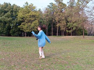 Beautiful young Chinese woman posing in sunny summer forest, wearing blue loose oversized top and miniskirt with small shoulder bag. Emotions, people, beauty, youth and lifestyle portrait.