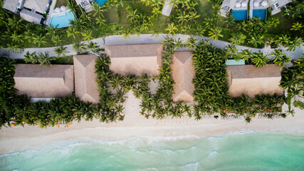 Aerial view of a tropical resort with thatched roofs, palm trees, and a turquoise beach, evoking a...