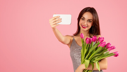 Vivacious woman with a captivating smile taking a selfie, holding a bouquet of pink tulips