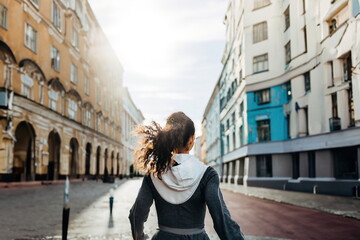 Fototapeta premium Back view of a young woman running in the morning in the city