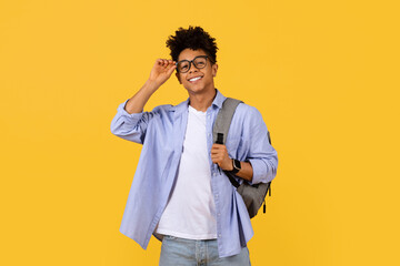 Confident black student adjusting glasses on a yellow background
