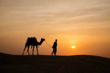 Fototapeta na wymiar Camel man and camel during sunset with colorful sky at Jaisalmer sand dunes, Rajasthan, India, Asia. Background. Backdrop. Wallpaper.