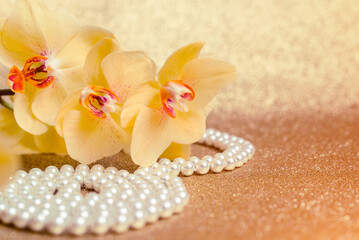 yellow Orchid and pearl necklace on a shiny gold background
