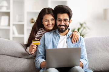 Millennial couple using computer and credit card at home