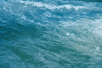 Bluewater waves on the surface ripples blurred. Defocus blurred transparent blue colored clear calm water surface texture with splash and bubbles. Water waves with shining pattern texture background.