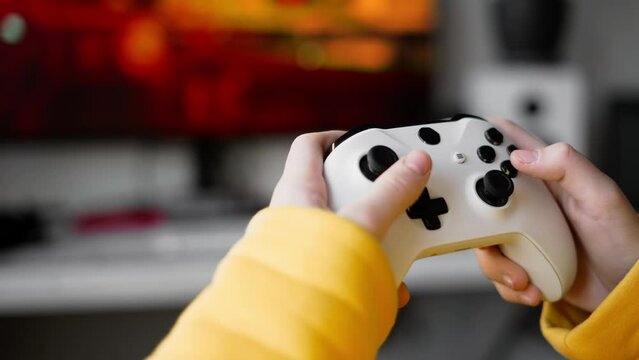 The teenager holds a large white gamepad in his hands and actively presses buttons. Close-up of the hands. Live Hand Held shooting