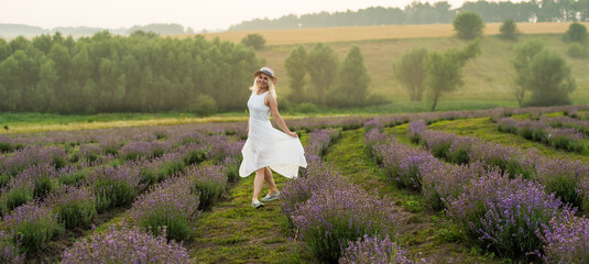 Beautiful young woman wearing a white dress walking in the middle of a lavender field in bloom