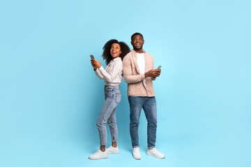 Excited african american couple with phones on blue background