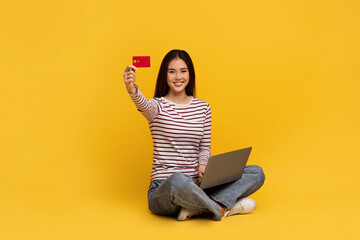 Cheerful young asian woman holding laptop and credit card - obrazy, fototapety, plakaty