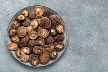 Obraz na płótnie Canvas Dried shiitake mushrooms on a plate, gray concrete background. Top view, flat lay.
