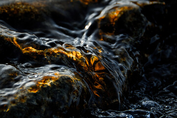 Wasser eingefroren über einem Stein. Gold leuchtend. Oberflächenstruktur. Welle gleitet über...