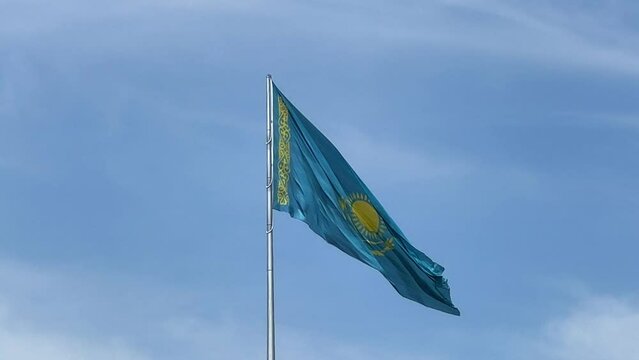 The flag of Kazakhstan is flying in the wind. Astana - Nur Sultan. A waving flag on a flagpole against the blue sky in Kazakhstan. The flagpole of the Republic of Kazakhstan on a bright sunny day. 4K 