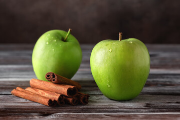 Green apples and cinnamon sticks on a old wooden table. Side view, selective focus.