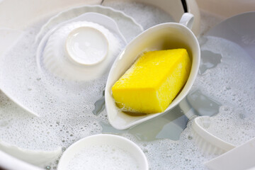 Dirty dishes with cleaning sponge in foam of dishwashing liquid. Washing dishes concept
