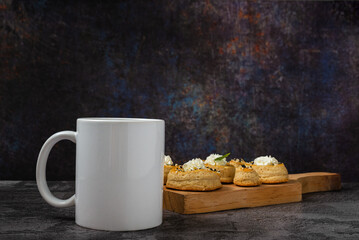 White cup with puff pastry rolls in the background on wooden table. Breakfast concept.