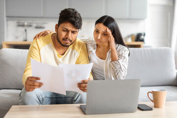 Bad News. Upset Indian Couple Reading Papers, Sitting On Couch At Home