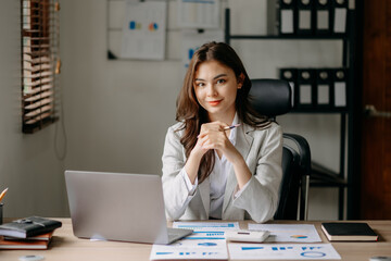 Young Asian businesswoman working with working notepad, tablet and laptop documents talking on the smartphone, tablet and laptop video call tax, report, accounting in the office