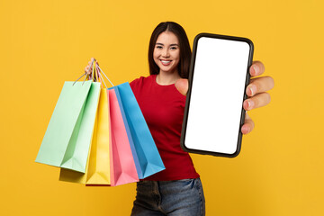 Cheerful young asian lady with purchases showing huge phone
