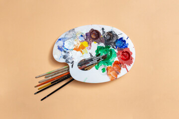 Painter palette with multiple smudged colors and brushes on beige background, abstract texture