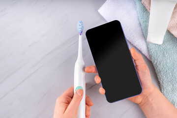 Electric Toothbrushes concept. Ultrasonic tooth brush with smartphone, with cosmetics bottles, stack of towels, toothpaste and phone. Female girl hands in pic. Modern dental care technology