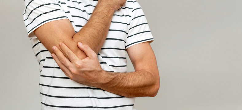 Joint pain, elbow pain, man holds his elbow with his hand closeup photograph. 