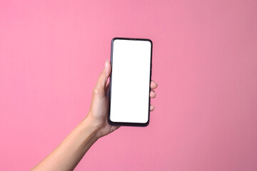 Fototapeta na wymiar Female hand holding smartphone with white blank phone screen for mockup on pink background