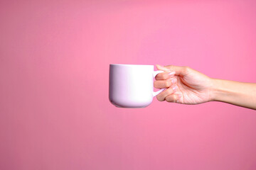 Woman hand holding white blank coffee cup mockup isolated on pink background