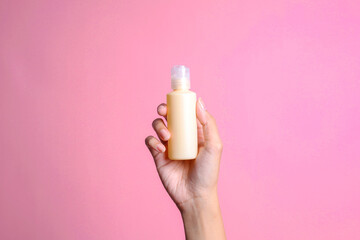 A woman's hand elegantly holds a cream mockup bottle on a pink background
