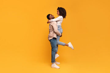 Black man lifting woman in joyful embrace, full length