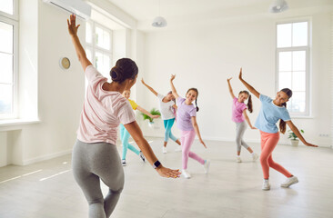 Happy children having dance class with woman teacher. Kids learning some ballet like moves. Group of little girl dancers rehearsing new choreo in spacious light white room at modern gym or dance hall