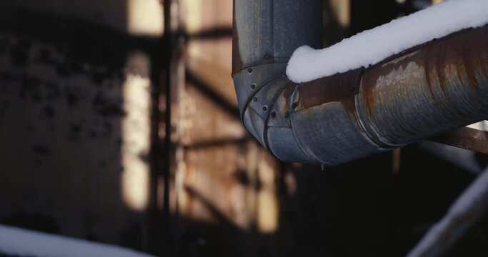Snowy pipe in an abandoned industrial factory. Rusty metal surfaces in the background. Slow camera movement
