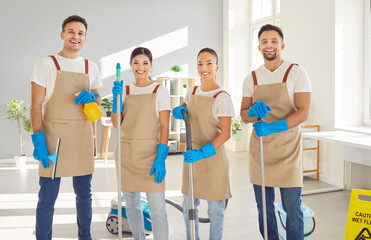 Portrait of happy smiling team of young janitors in uniform from professional cleaning service...