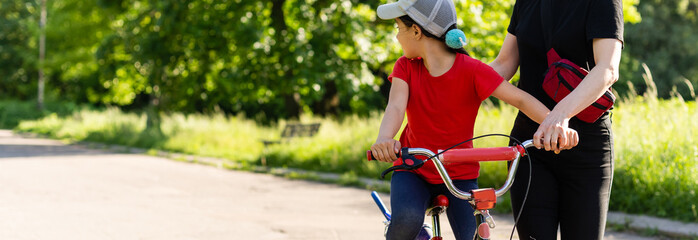 Beautiful and happy young mother teaching her daughter to ride a bicycle. Both smiling, summer park...