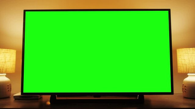 Zoom in of a horizontal green screen TV. Cozy evening living room.
