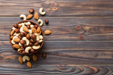 Fototapeta na wymiar Assortment of nuts in wooden bowl on colored table. Cashew, hazelnuts, walnuts, almonds. Mix of nuts Top view with copy space