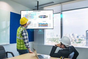 Talking with a male engineer at an office meeting, a confident male manager is viewing an interactive digital whiteboard TV that displays new environmentally friendly and sustainable