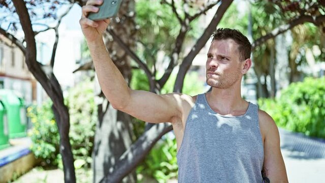 Smiling man taking selfie in sunny park with trees and bench