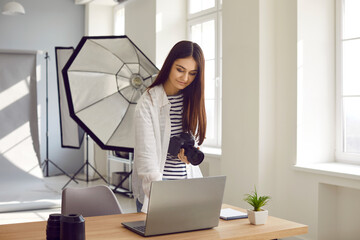 Portrait of a young happy smiling woman photographer with camera and lenses on her workplace...